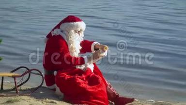 圣诞老人坐在湖边的沙滩上，拿着一个礼品袋，把一些东西写在清单上。 度假村的圣诞老人