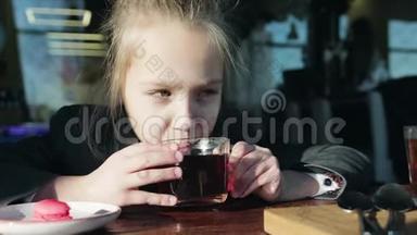 可爱，小女学生坐在桌子旁吃马卡龙，喝茶。 女孩吃健康食品