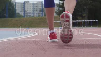 一名年轻女子运动员在慢动作训练中开始在城市田径跑道上奔跑的红色短腿
