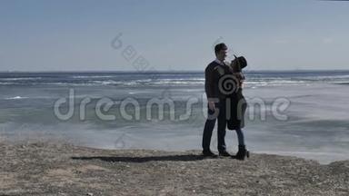 一对年轻夫妇走在岩石海岸上，靠近一条<strong>冰封</strong>的河