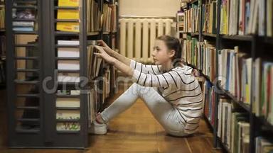 女孩在图书馆的书架上选择了一本书。 坐在图书馆地板上的女孩