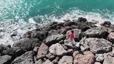 穿着红色漂亮衣服的女人，双手分开，站在岩石峭壁海滩上，海浪拍打着岩石，溅起水花