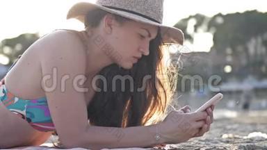 一个女人在海滩上用智能手机发短信，背景是大海