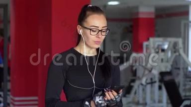带着耳机的年轻<strong>女孩</strong>在健身房里用智能手机。 <strong>女孩听音乐</strong>