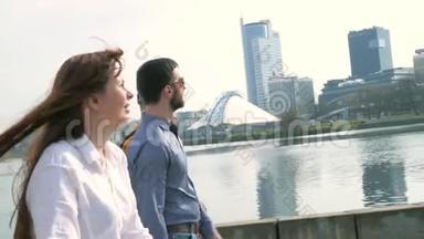 年轻漂亮的女人和三个男人正在沿着城市的堤坝走，背景是高楼大厦