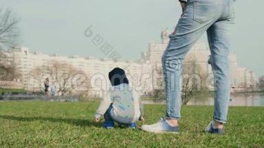 小男孩蹲在草地上玩，背对着镜头坐着，小妈妈站在他<strong>身边</strong>