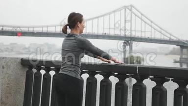 年轻漂亮的运动装女人在跑步训练前正在城市码头上伸展。 穿<strong>漂亮衣服</strong>的黑发女子