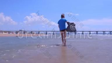 海上度假的小男孩穿着湿t恤在沙滩上的海水中散步。