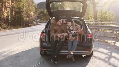 可爱的，年轻的夫妇喝热茶从热水瓶坐在汽<strong>车后备箱</strong>。 快乐的白种人夫妇喝咖啡