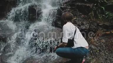 女徒步旅行者蹲伏在飞溅的丛林瀑布中