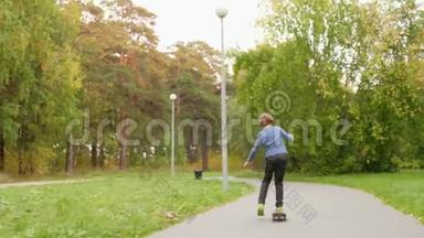 美丽的绿色公园里可爱的十几岁男孩骑滑板的后视镜。