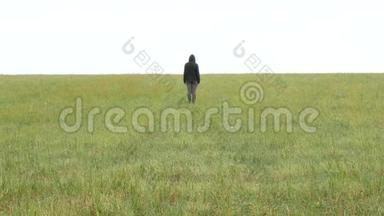 身穿卡其色运动服和头罩的女孩站在地平线上的草地上