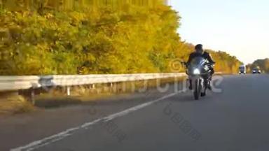 在秋高气爽的高速公路上骑着现代摩托车的年轻人。 摩托车手在乡间公路上骑摩托车