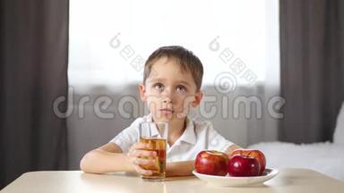 一个小男孩坐在桌子旁喝果汁。 快乐的孩子笑了。 儿童健康食品的概念