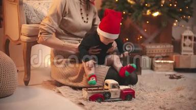一个年轻的微笑的女人，戴着红<strong>帽子</strong>和她的小<strong>宝宝</strong>玩——在圣诞工作室里玩玩具车