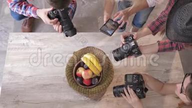 摄影师在一位主人的木桌上，在一个篮子里用数码相机和手机水果拍照