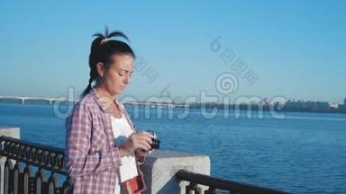 穿着衬衫的女人开着相机快门，在河堤上拍照
