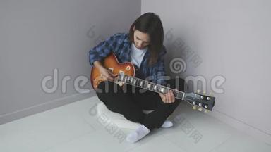 年轻可爱的女人坐在地板上弹电吉他练习音乐会。 漂亮的女人，用电吉他弹奏蓝色