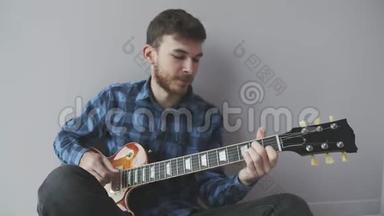 年轻的胡须英俊的吉他手独自弹吉他。 音乐家在电吉他上演奏，穿着蓝色衬衫。 音乐产业