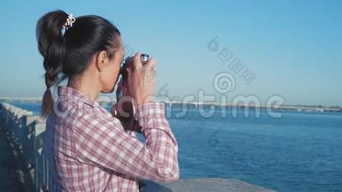 美丽的女人透过取景器观看河畔的复古相机