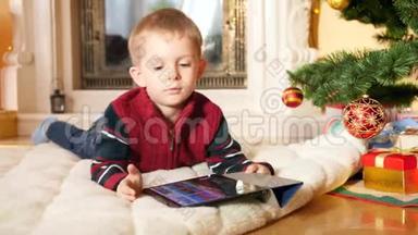 小男孩躺在圣诞树下的毯子上，在数字平板电脑上玩<strong>电子</strong>游戏的4k视频。 <strong>儿童</strong>