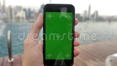 智能手机的特写镜头，绿色屏幕彩色键放在游泳池附近，在触摸屏上观看视频并跟踪