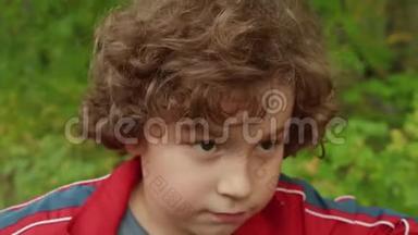 夏天公园的卷发黑发男孩的肖像。 在绿色公园里骑着自行车闭上脸的少年男孩。 英俊的男孩