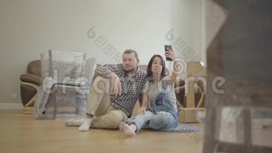 快乐的高<strong>加</strong>索夫妇坐在客厅的地板上，带着新的家具，打着<strong>视频</strong>电话。 微笑的一对