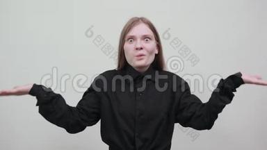不高兴的女人穿着黑色衬衫摊开双手，看着相机，困惑。