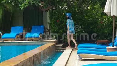 穿着蓝色泳衣，戴着帽子，戴着太阳镜的漂亮女士在游泳池里躺着一个阳光休息室，里面有清澈的水