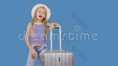 旅行女孩带着手提箱<strong>打招呼</strong>，在演播室的蓝色背景上<strong>打招呼</strong>。 带手提箱的少女