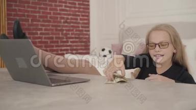 快乐的白人少女坐在她的房间里拿着笔记本电脑和零<strong>花钱</strong>。 双腿自信的女学生