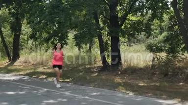 穿着粉红色衬衫和黑色短裤在公园里跑步的年<strong>轻运动</strong>女孩。 带着训练有素的身体做耳机的漂亮女人