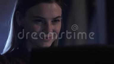 在笔记本电脑上工作，晚上使用电脑的年轻女子的肖像，脸上带着轻微的微笑，印着文字和文字