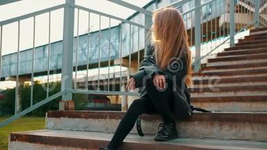 穿黑色<strong>皮夹克</strong>的少女坐在城市风景的楼梯上。 穿黑色<strong>皮夹克</strong>的时髦女孩