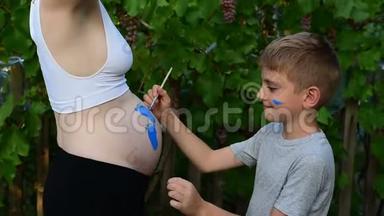 笑的男孩用刷子在他怀孕妈妈宝宝的肚子上画`脚印。 怀孕的概念。 特写