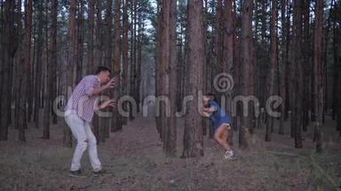 一家人在森林里玩得很开心，年轻的爸爸在假日里和小女儿在一排排松树之间玩耍