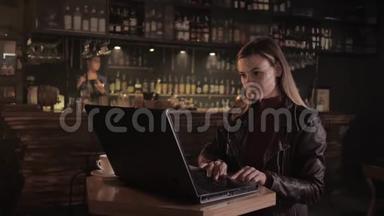 一位成功的女企业家坐在时尚酒吧的桌子旁，一边在电脑前工作，一边把胳膊搭在胸前