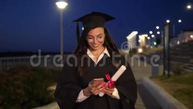 大学<strong>毕业生</strong>女孩带着文凭微笑，使用她的智能手机。