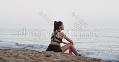 健康的生活方式概念：运动的女士在海边锻炼后，在海边喝干渴的水和