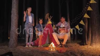 家庭的乐趣，快乐的父亲为妈妈弹吉他，女儿在夏季周末在篝火旁跳舞。