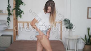 年轻女子站在卧室里，在腿上涂防纤维素奶油