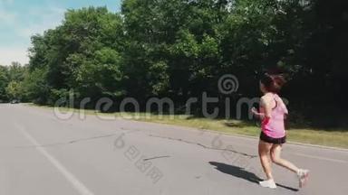 戴着耳机和粉红色衬衫的漂亮运动女跑步运动员正在城市公园训练。 苗条的白种人女人在跑步。 Y：