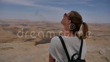 年轻女子背着背包站在悬崖边`望着天空转身