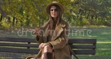 美丽的高加索女人，戴着太阳镜和优雅的衣服，喝着茶或咖啡，环顾四周。 美丽美丽