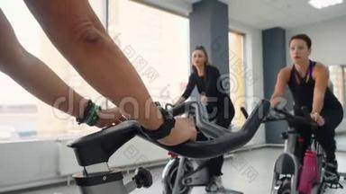 在健身俱乐部的自行车健身房，妇女团体旋转自行车。 健身妇女骑自行车训练。 女运动员手