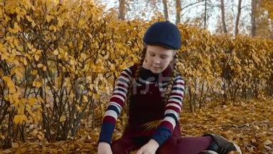可爱的少年女孩，红头发辫，在秋天的公园里扔黄叶。 快乐的女孩把落叶从