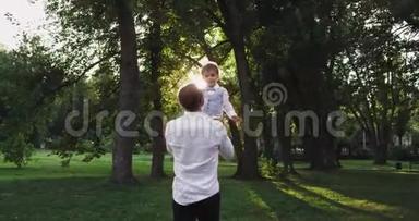 可爱的小男孩和他的爸爸在绿色公园中央的日落时玩得非常可爱，一起享受着这一刻