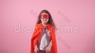 漂亮的小卷发女孩，穿着红色英雄套装，戴着粉红色背景的面具