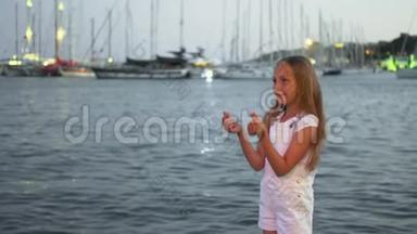 在傍晚的海港风景中，一个在风中挥动头发的少女。 在海上和游艇背景下许愿的快乐女孩